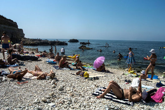 Туристи се препичат под яркото слънце на плажа Тийнейджъри скачат
